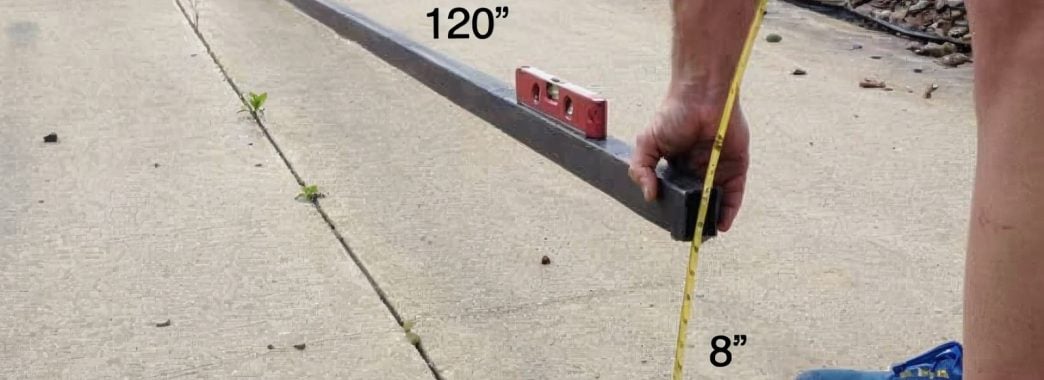man measuring grade with a level, tape measure, and straight material